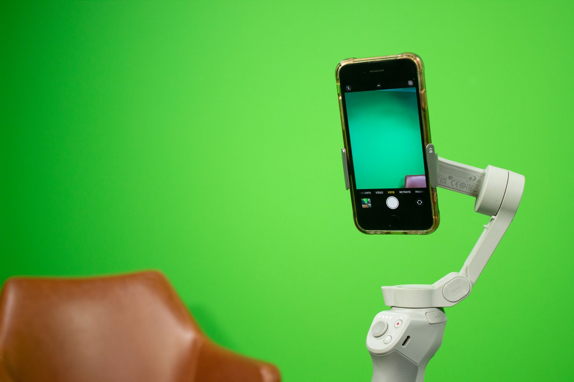 Un smartphone fixé sur un stabilisateur devant un fond vert, avec un fauteuil en cuir flou au premier plan